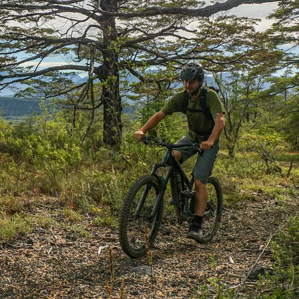H+I Guide Luc pedalling his mountain bike uphill with green bushes and trees in the background
