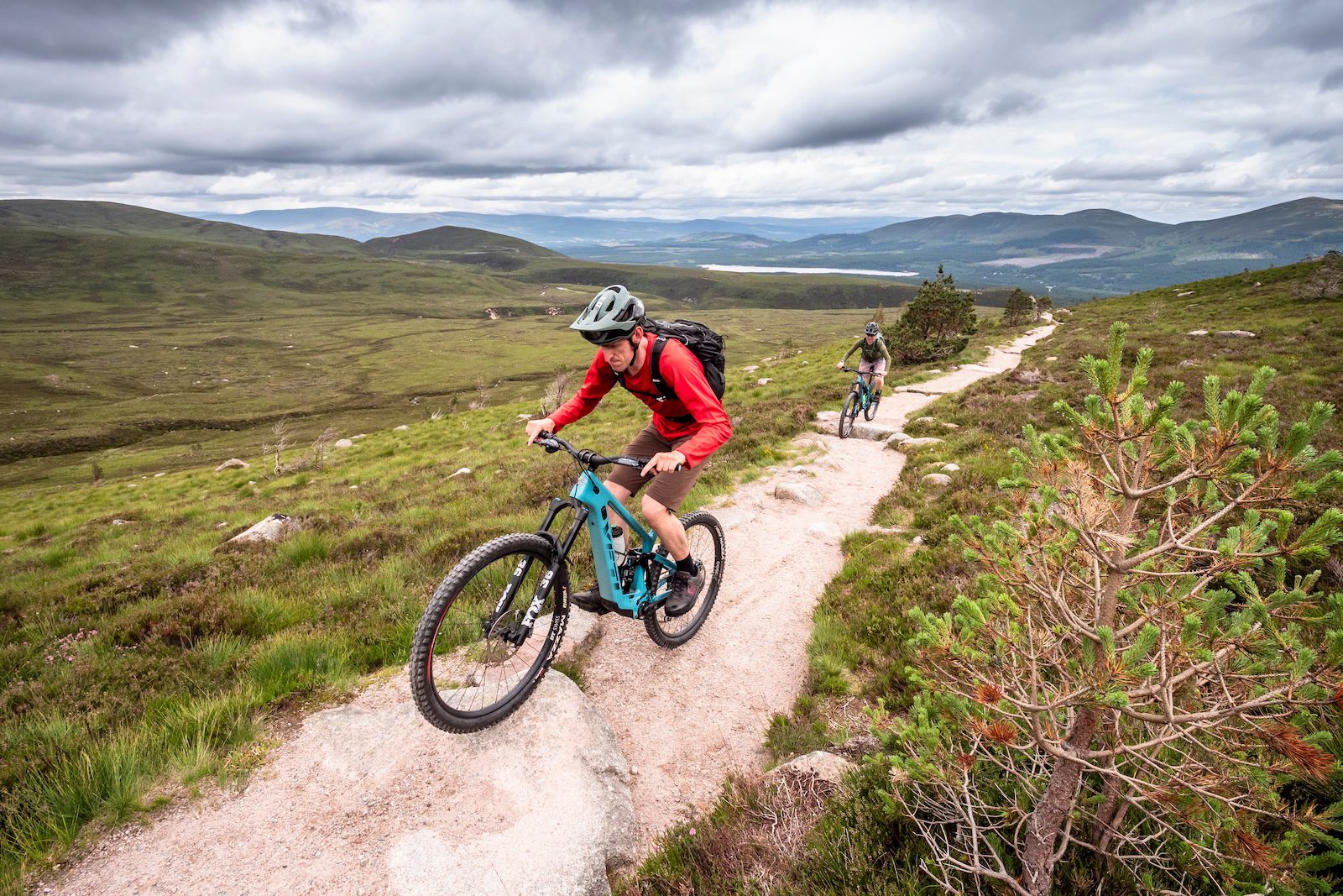 E-mountain biker and mountain biker riding up a climb in the Cairngorms