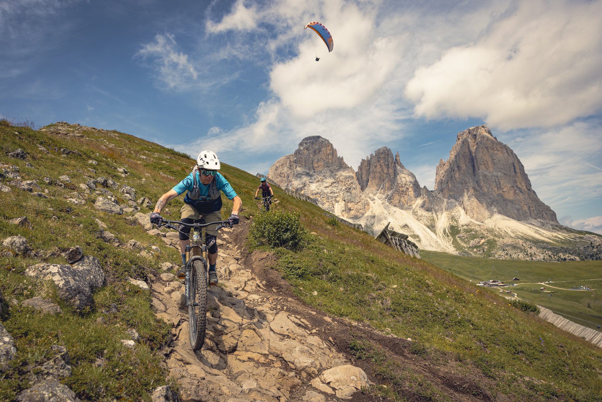Male and female mountain bikers and paraglider in the Dolomites