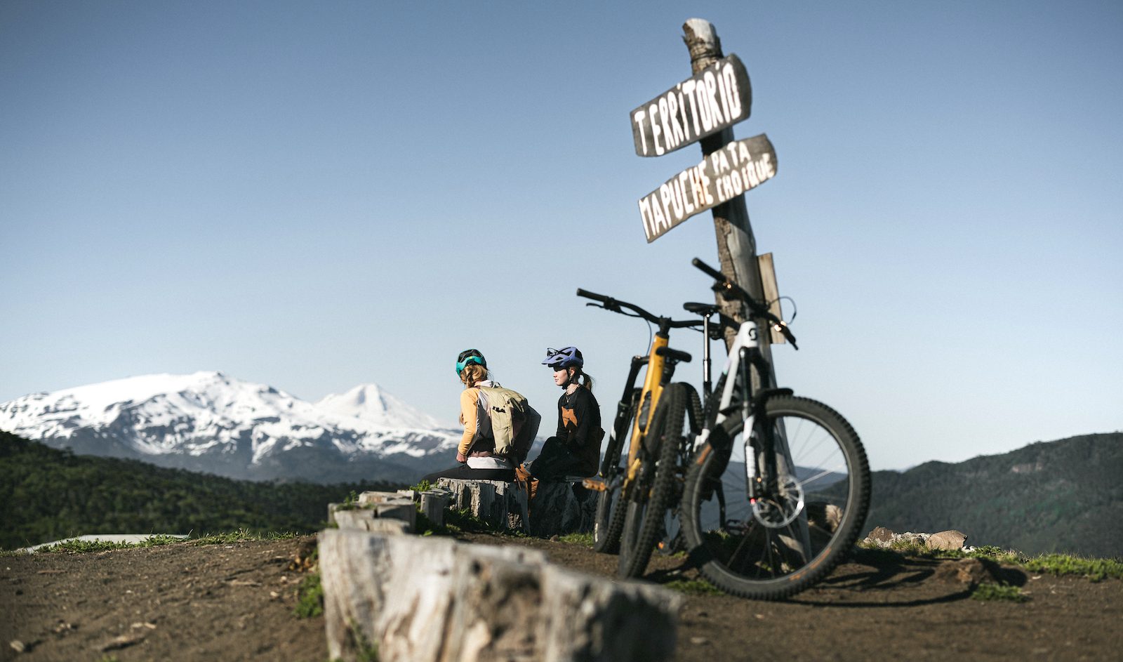 Two female riders look out over the vast landscape of the Andes after their pedal to the top
