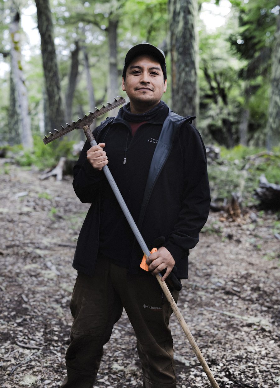 A Mapuche man stands with his trail tool after clearing the leaves from a section of singletrack