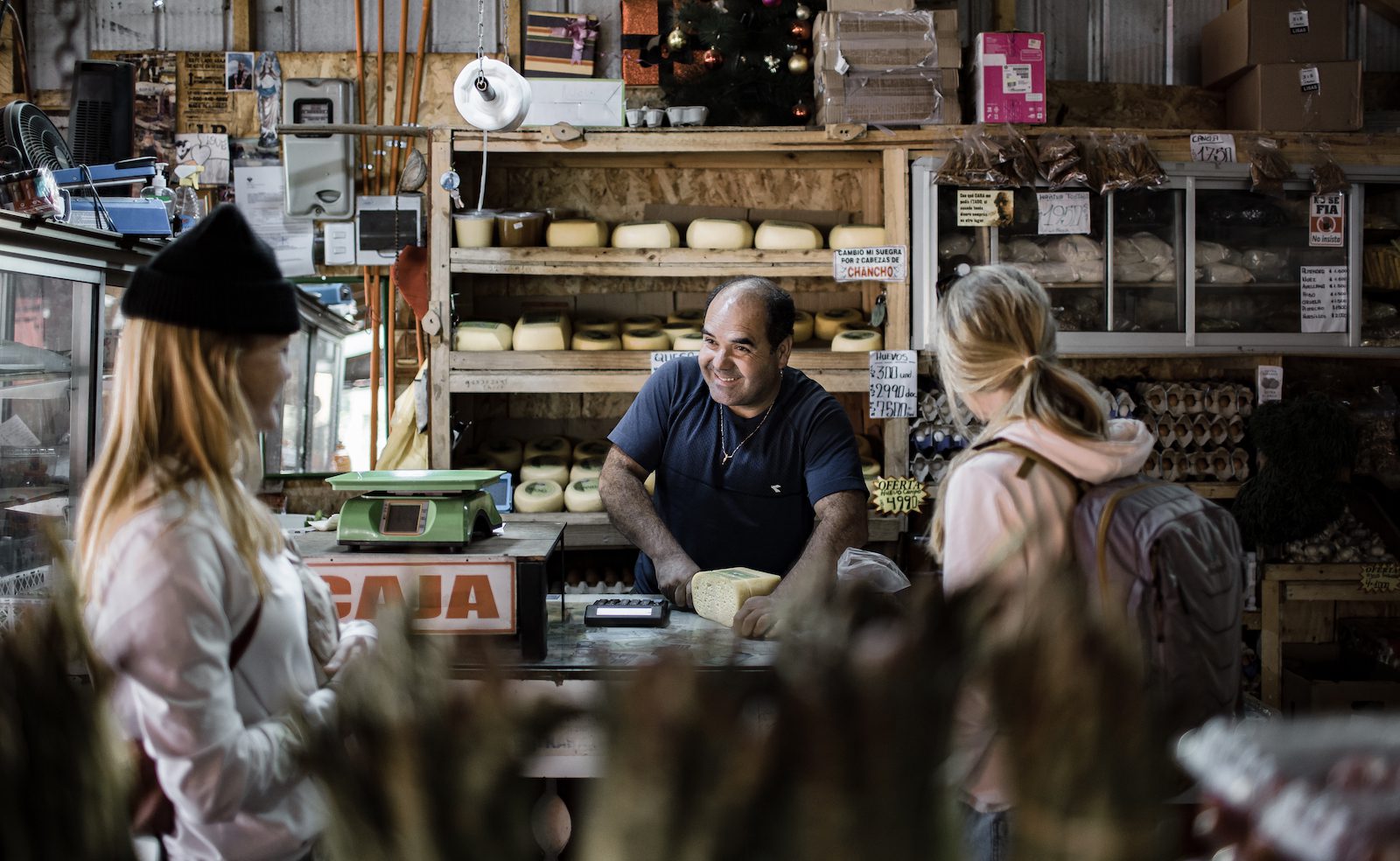 A local artisan cheese maker cuts a slice from a block while smiling at two customers