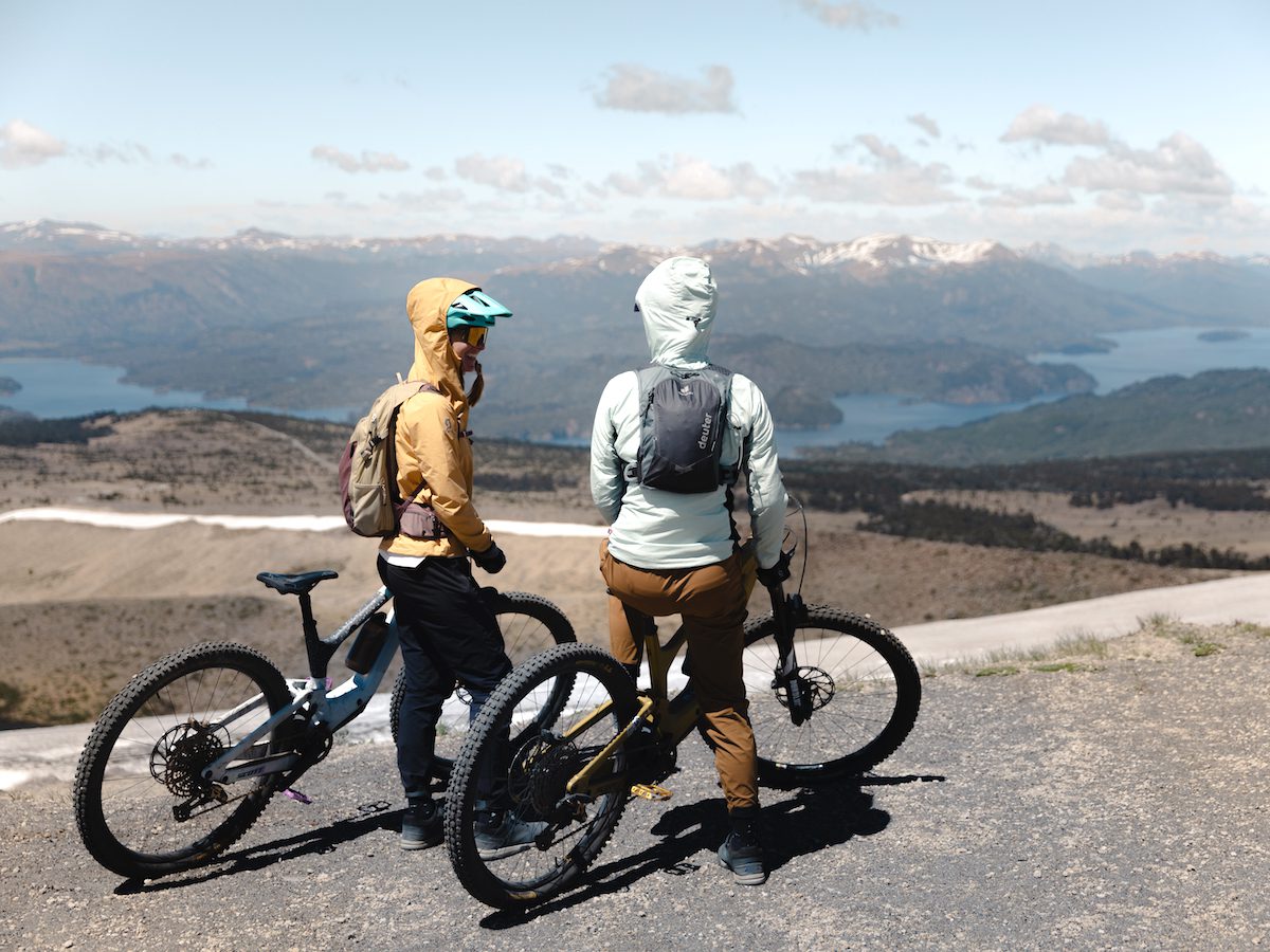 Two female e-mountain bikers smile as they look out over the lakes and volcanoes region of Chile