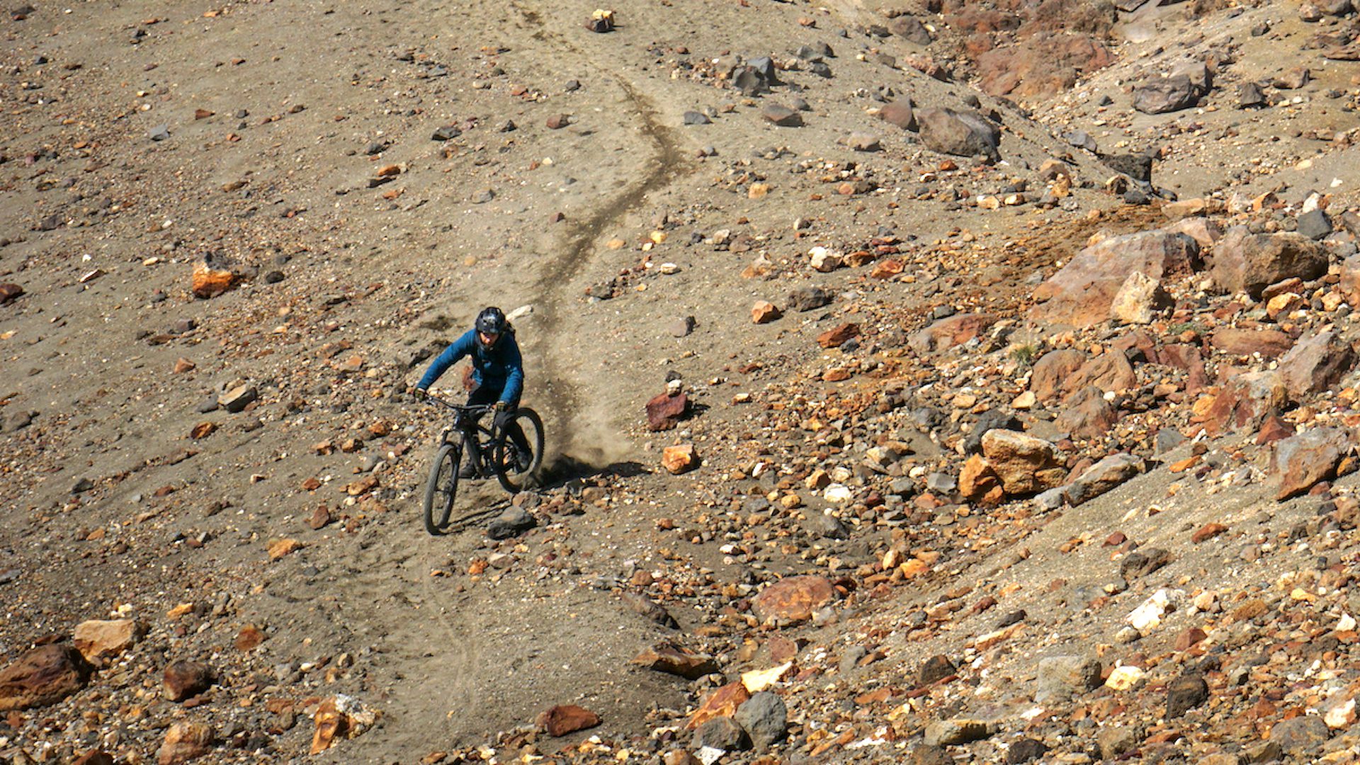 Mountain biker descending a steep and loose trail and navigating through boulders.